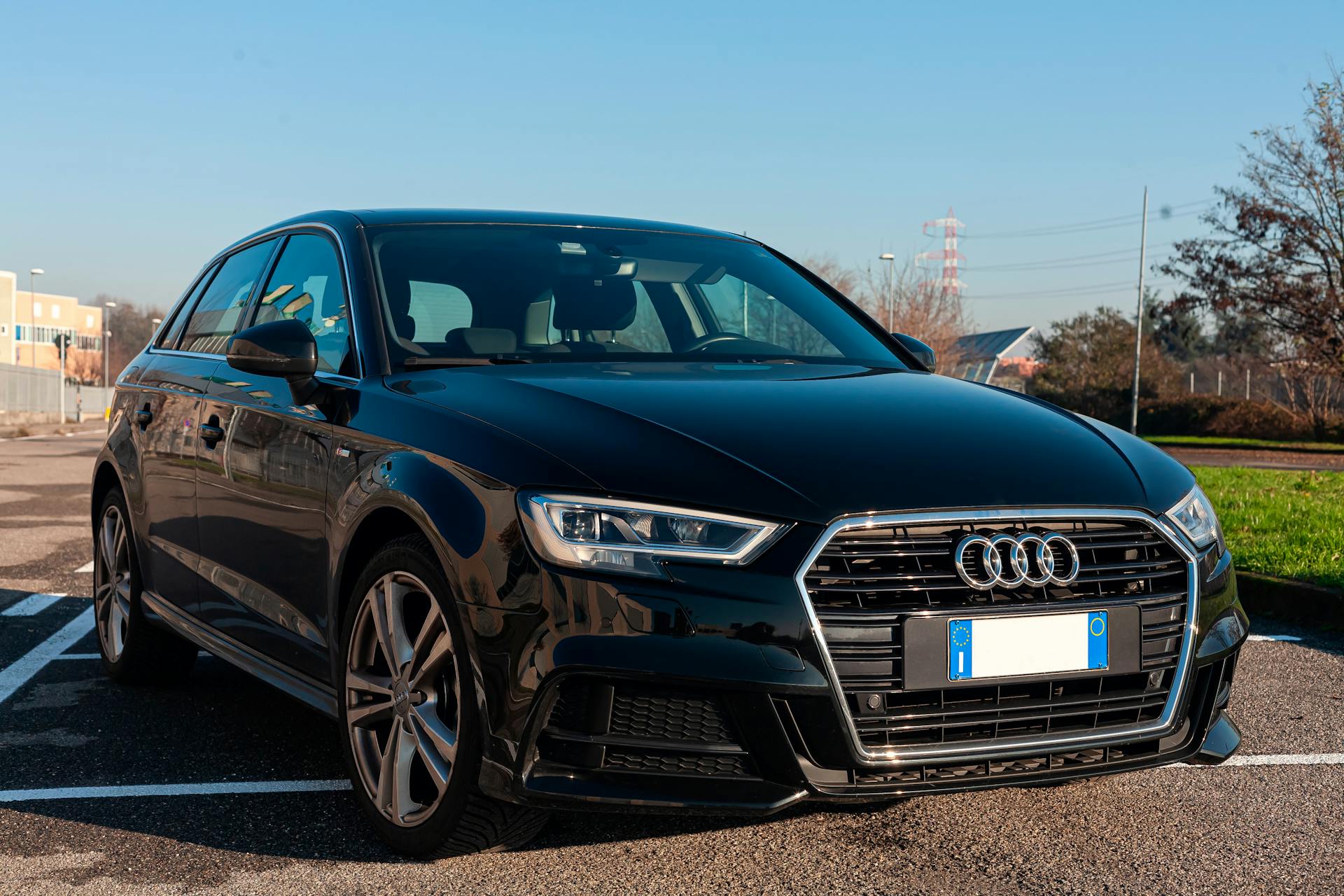 A stylish black Audi parked outdoors under a blue sky in Milan, Italy.