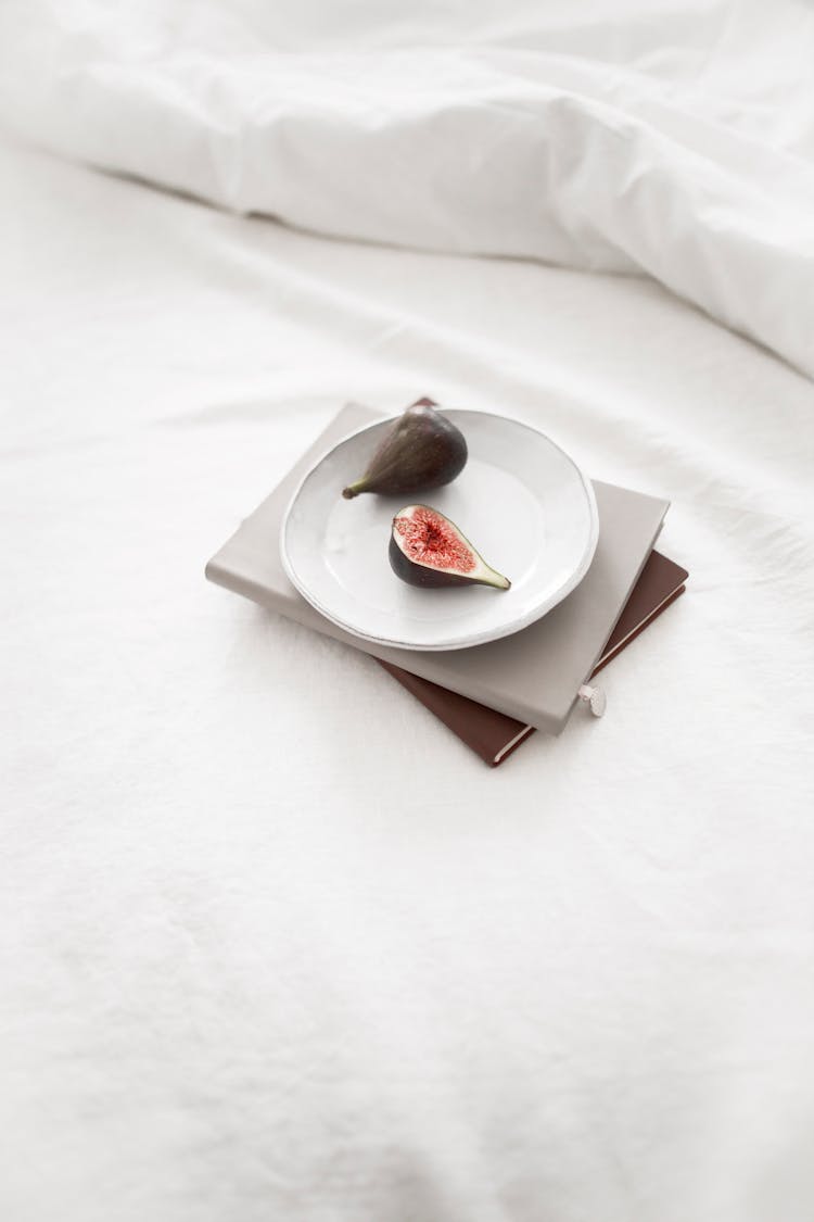 Plate Of Fig Fruit And Books Placed On Soft White Bed