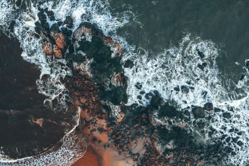Free Drone view of rocky formations on shore near sandy beach and wavy sea in summer day Stock Photo