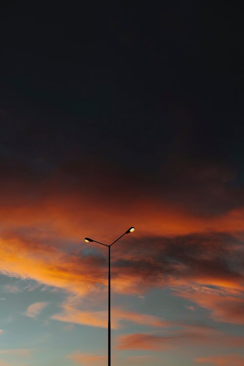 Free A silhouetted streetlight stands against a vivid orange and dark sky at twilight. Stock Photo