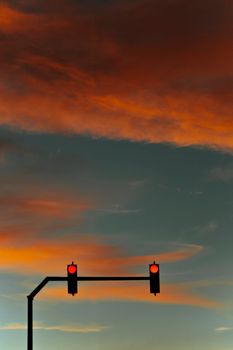 Red traffic light silhouetted against a vibrant sunset sky with orange clouds.