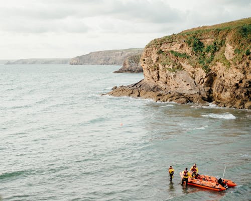 Anonymous rescuers standing in sea near boat against overcast sky