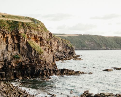 Free Rough cliffs covered with green grass located on rocky shore of wavy ocean against cloudy sky Stock Photo
