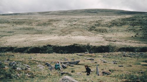 Free Unrecognizable female travelers walking on grassy meadow near hill slope under gray dramatic sky in mountainous countryside Stock Photo