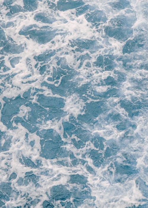 Top view of foamy water of blue sea with white waves in sunny weather in summer