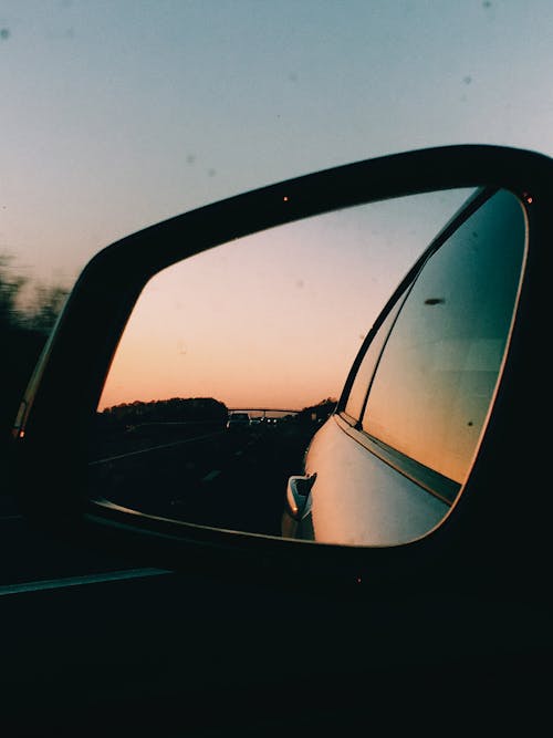 Bright sundown sky over asphalt highway and trees through mirror of modern automobile