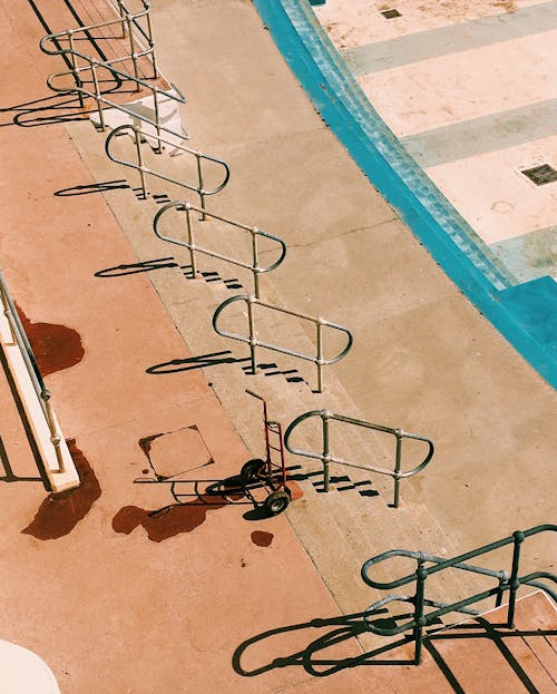 High angle of stairs near trolley and metal railings near empty waterless pool with dirty spots in sunny summer day in street