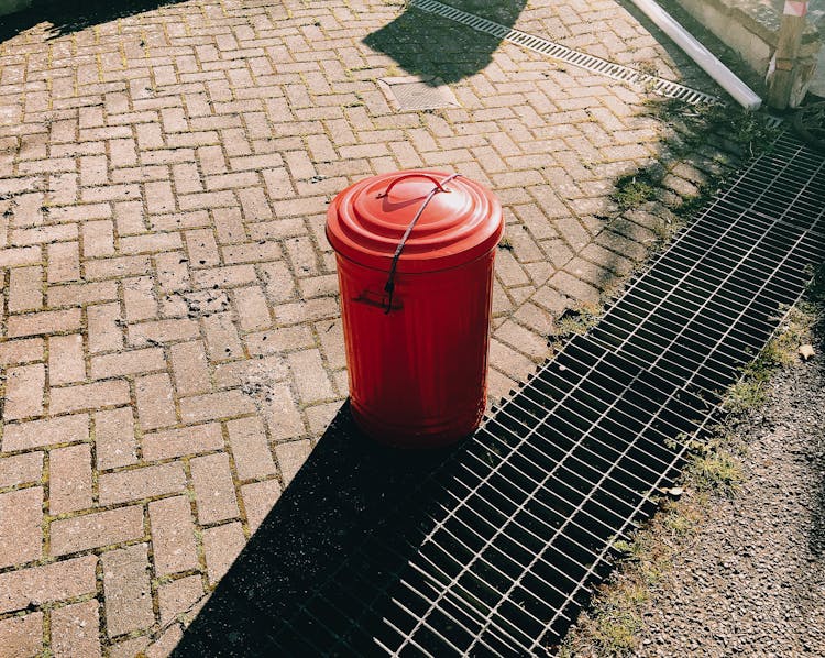 Red Trash Can On Pavement Near Sewer Grates