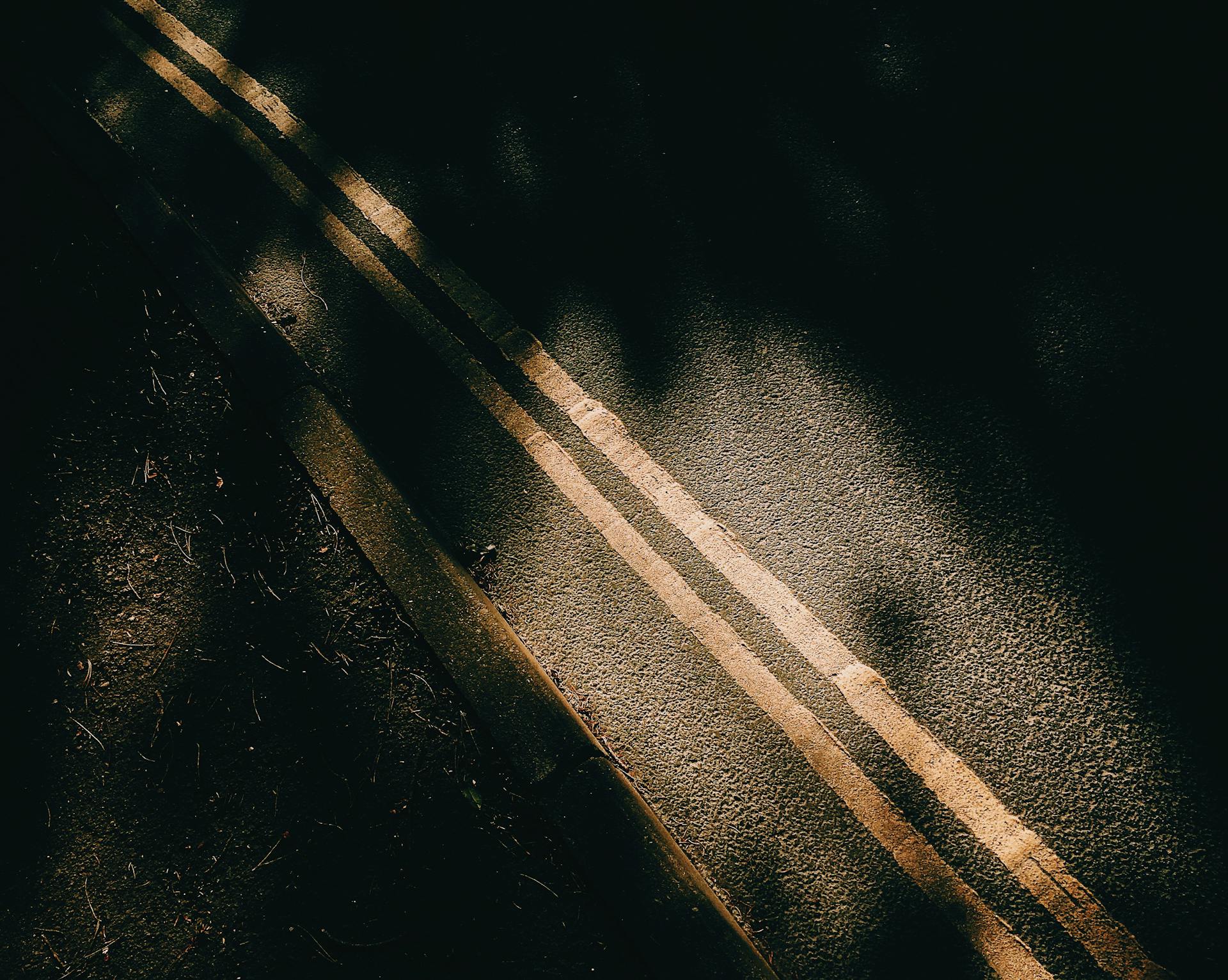 From above of asphalt roadway with yellow marking lines with dark shades near ground in sunny day in street