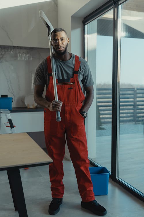 A Man Wearing an Orange Overall Posing with a Cleaning Tool