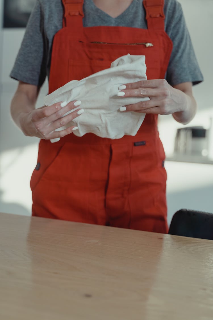 A Cleaner Wearing An Orange Overall Holding A Rag