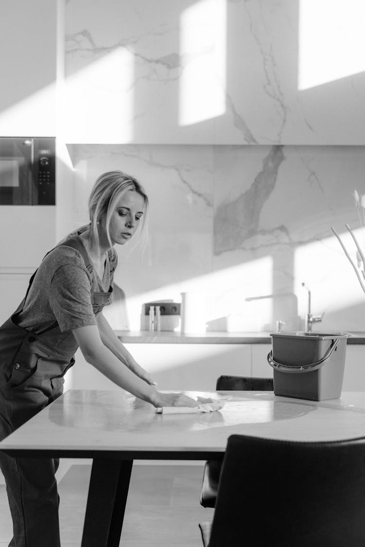 Grayscale Photo Of A Woman Wiping A Table With Wet Rag