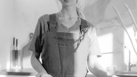 Black and white portrait of a housekeeper with cleaning supplies in a modern kitchen.