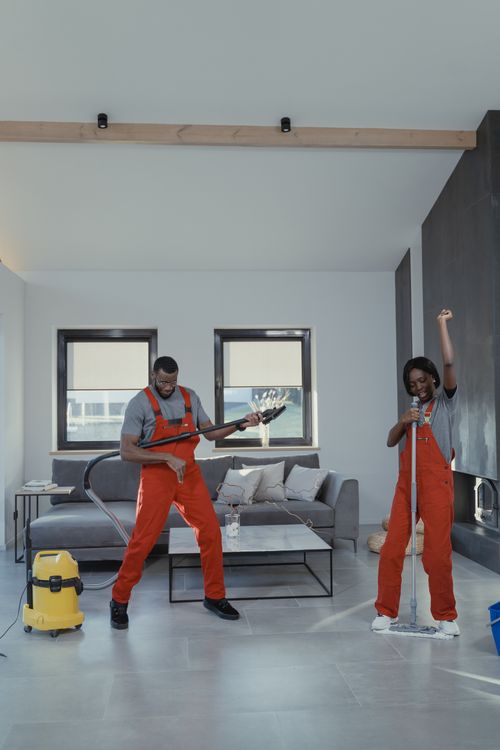 Free Two cleaners enjoying work, pretend playing musical instruments with cleaning tools in a modern living room. Stock Photo