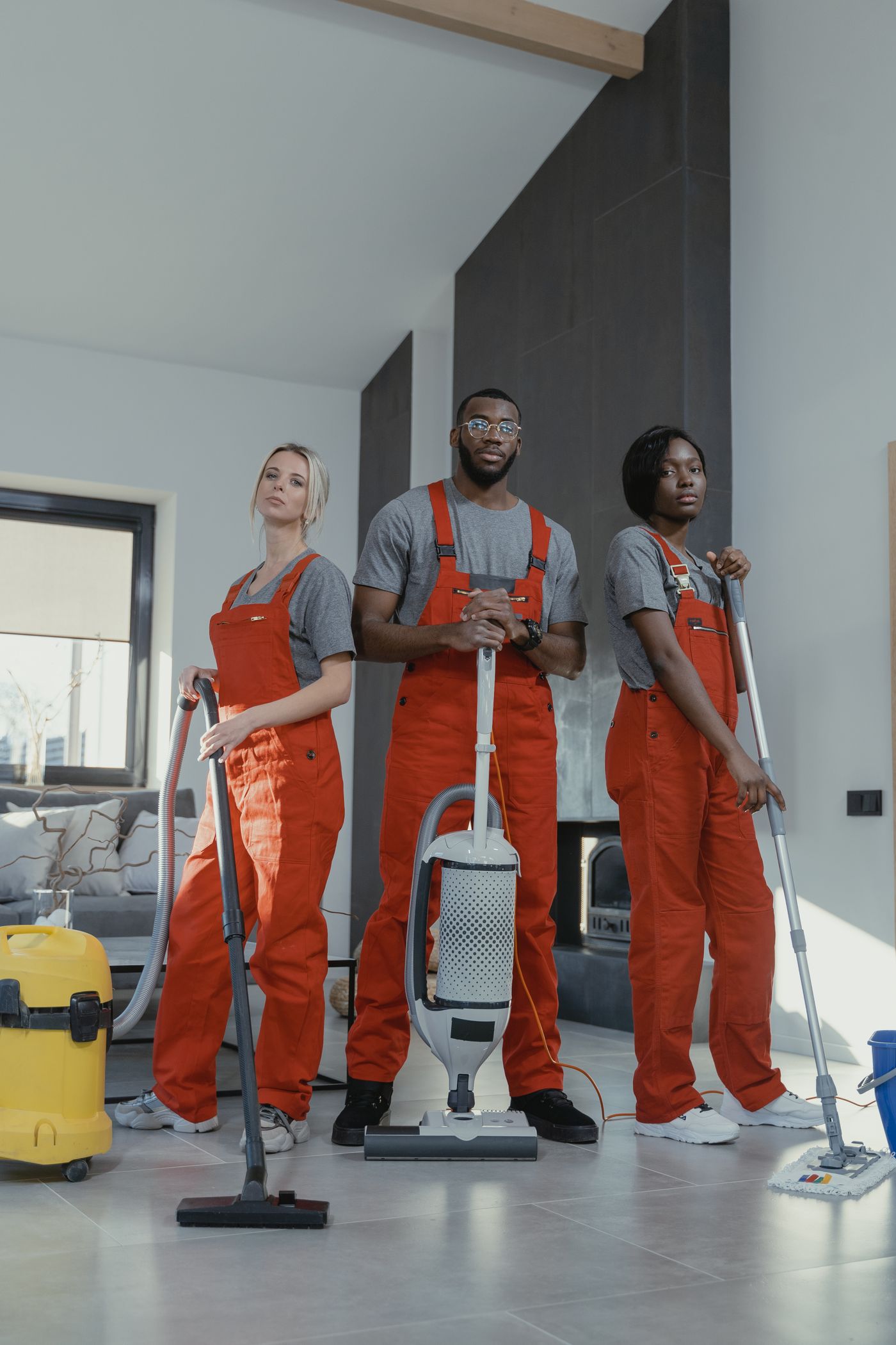 Equipo de Brilla, tres limpiadores con peto naranja y su material, en un salón luminoso de Madrid