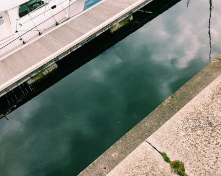 High angle of shabby stone surface near wooden pier with moored white boat on water in daylight in town harbor