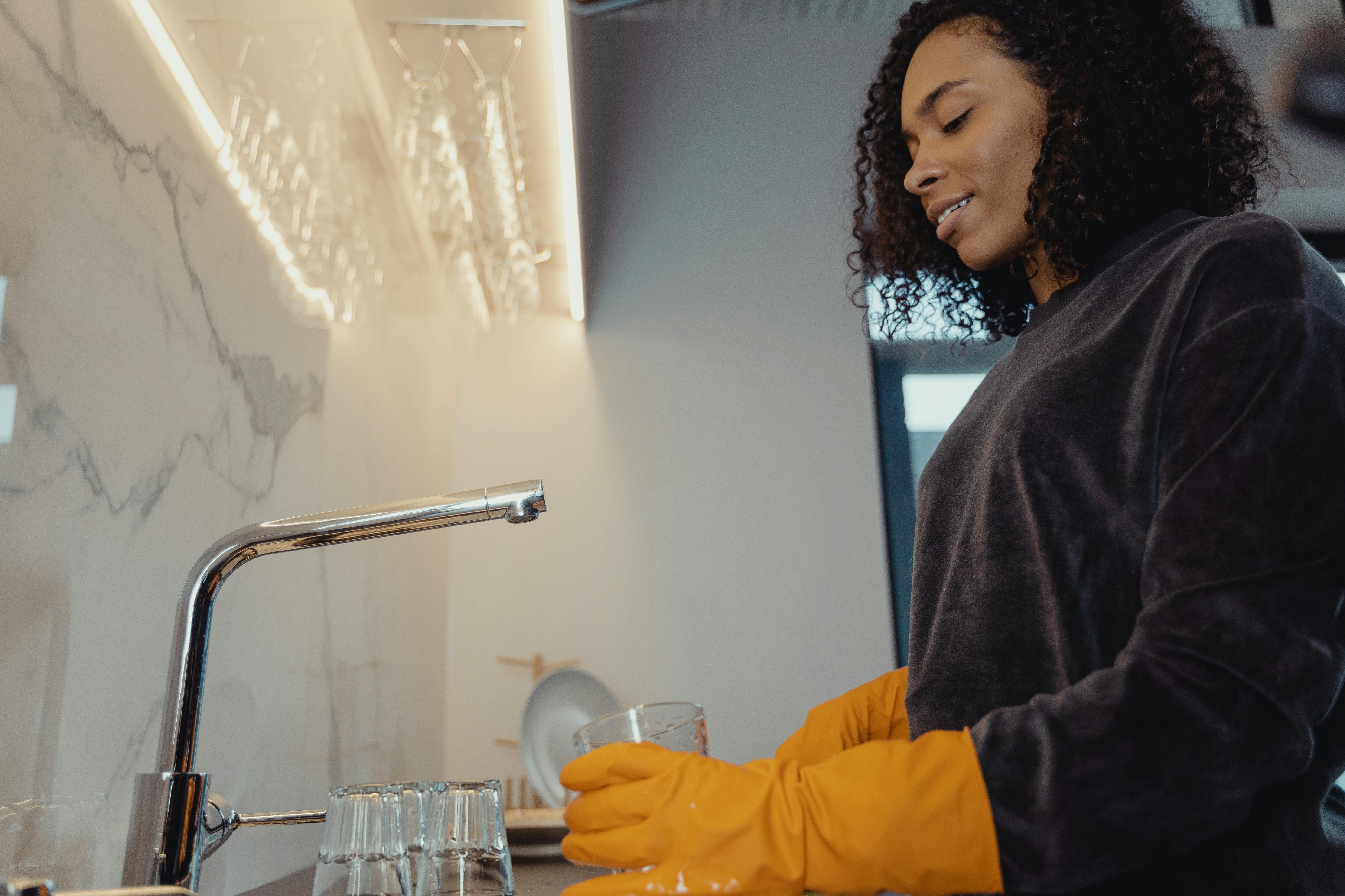 Cam sehpa üzerindeki dairesel bardak lekesini mikrofiber bez ve temizlik spreyi kullanarak temizleyen kişi.