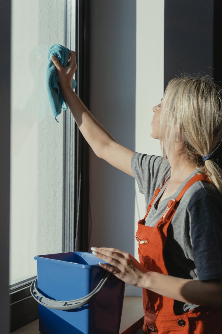 Woman In Gray Shirt Wiping The Glass Window