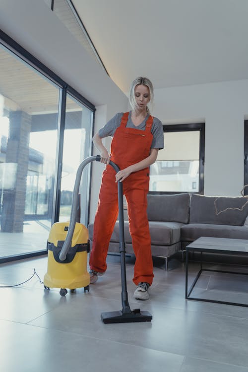 Woman in Blue Shirt and Orange Pants Holding Vacuum Cleaner