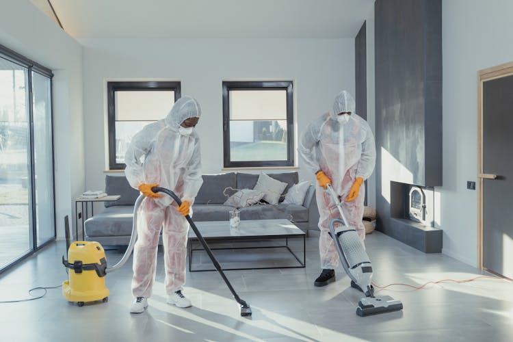 Cleaners In PPE Vacuuming A Tiled Floor