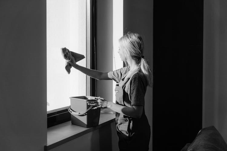 Grayscale Photo Of Woman Wiping The Window