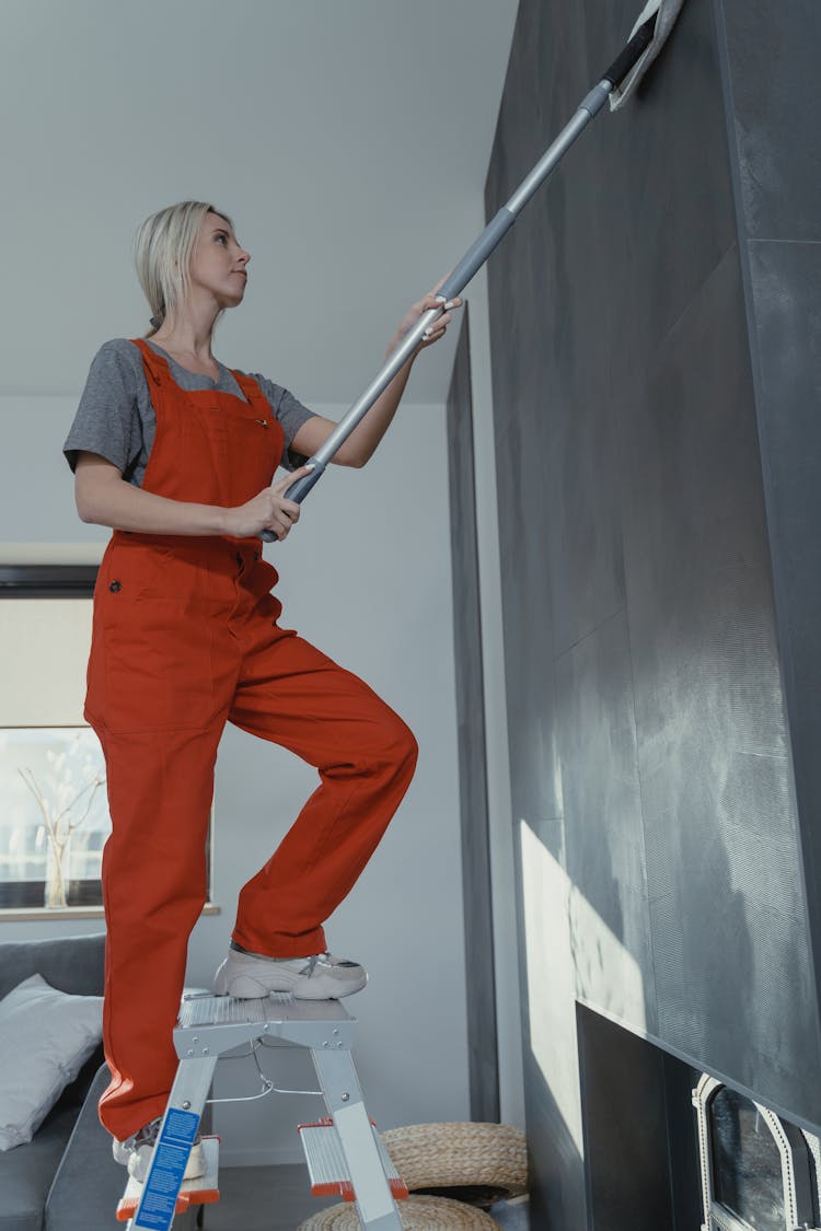 Woman Wiping The Wall While Standing On A Ladder 