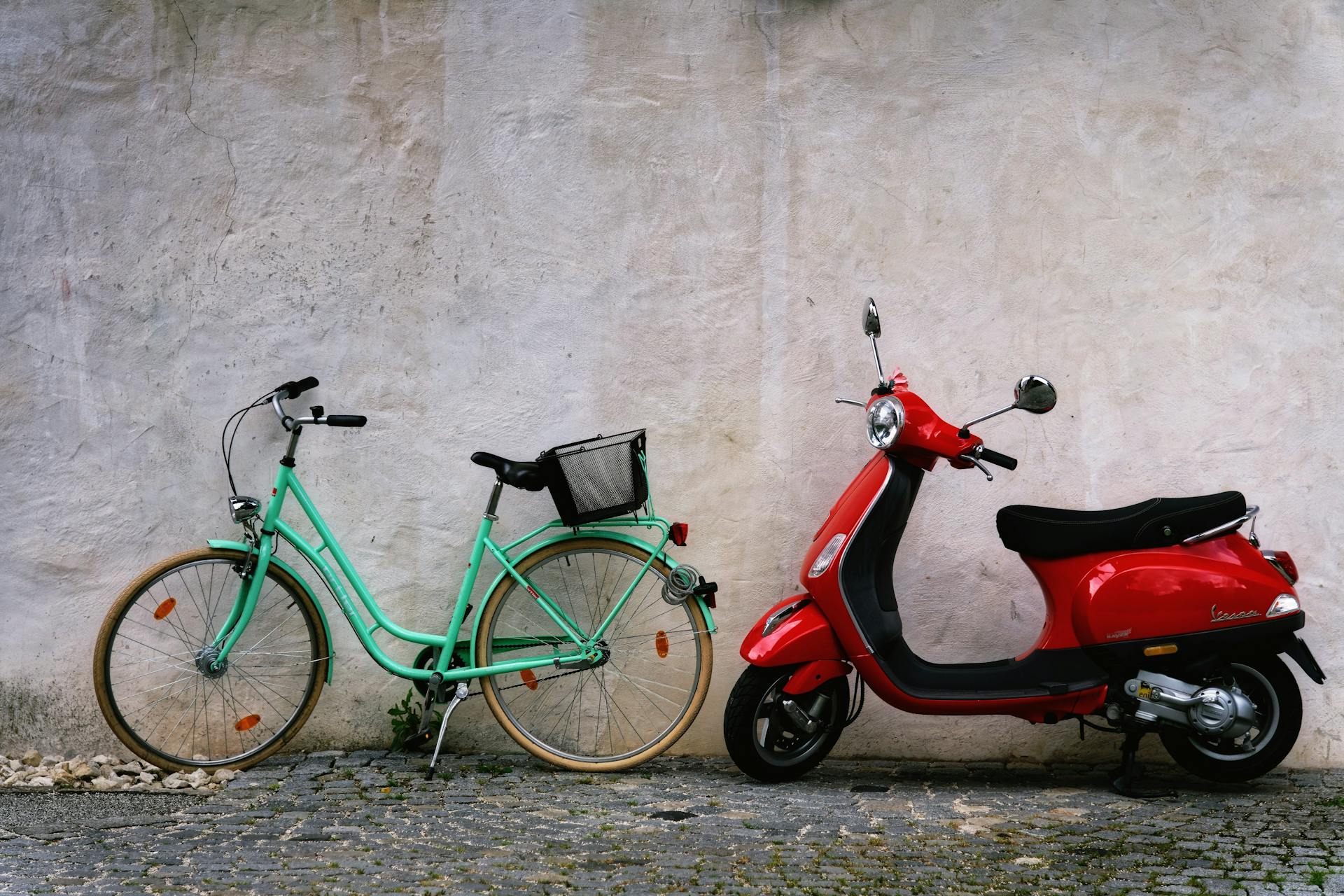 Parked bicycle and scooter side by side in front of a rustic wall, showcasing urban transportation options.