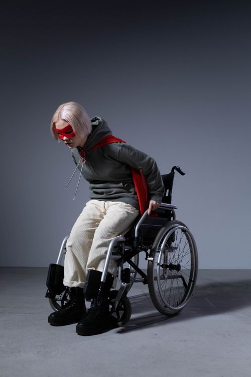 Free Teenager in wheelchair with red cape embodying strength and courage in studio setting. Stock Photo