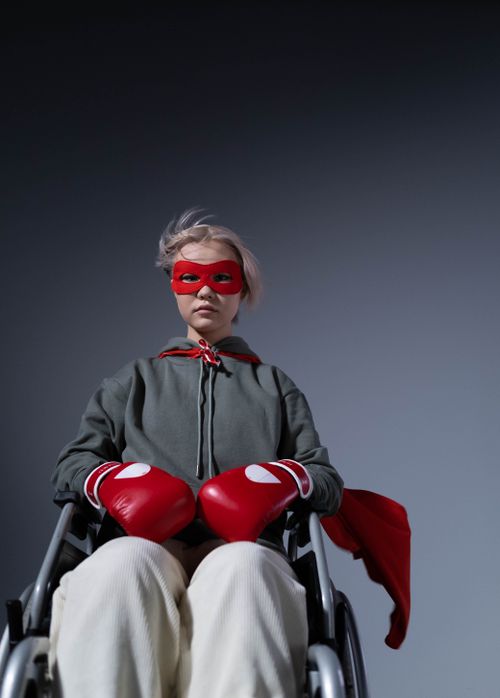 Free Teen in wheelchair wearing superhero cape and boxing gloves, symbolizing strength and empowerment. Stock Photo