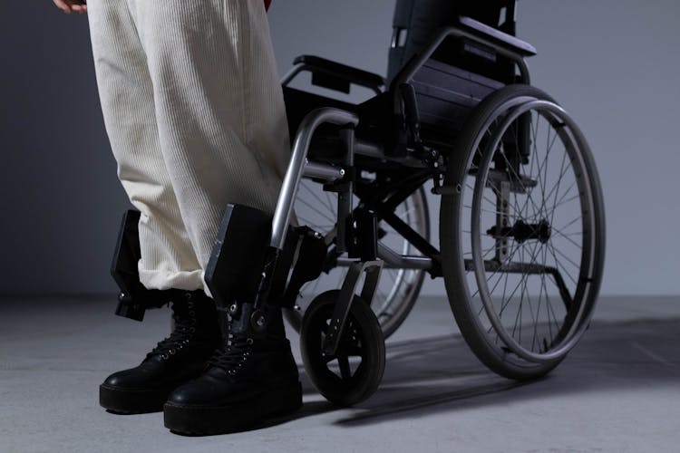 Person Wearing Black Boots Standing In Front Of A Wheelchair