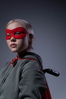 Portrait of a teenage girl in superhero costume with red mask and cape in studio setting.