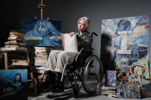 An artist in a wheelchair in her studio, surrounded by vibrant artworks and books.