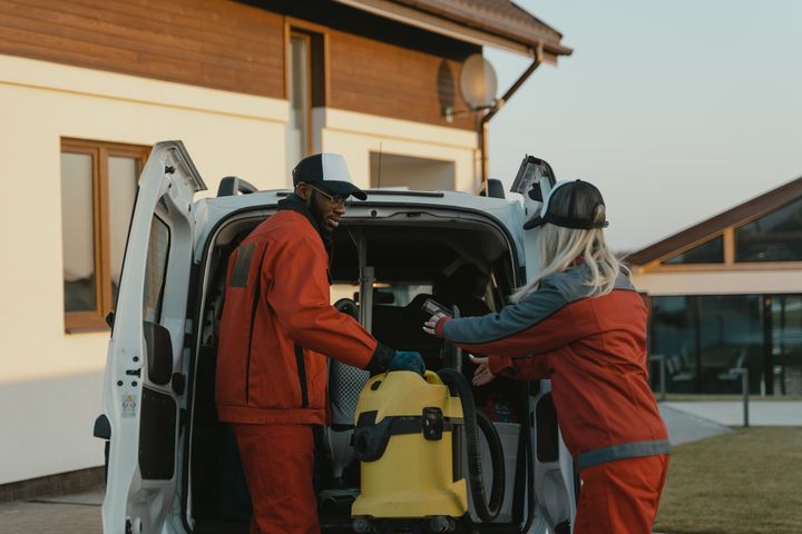 Two cleaners loading a wet vacuum into the back of a work van
