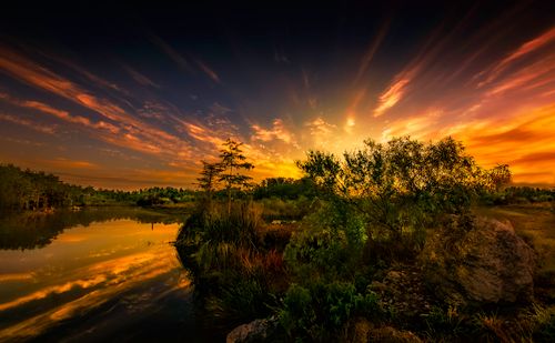 Free A breathtaking sunset casts vibrant colors over a peaceful lake surrounded by lush trees and nature. Stock Photo