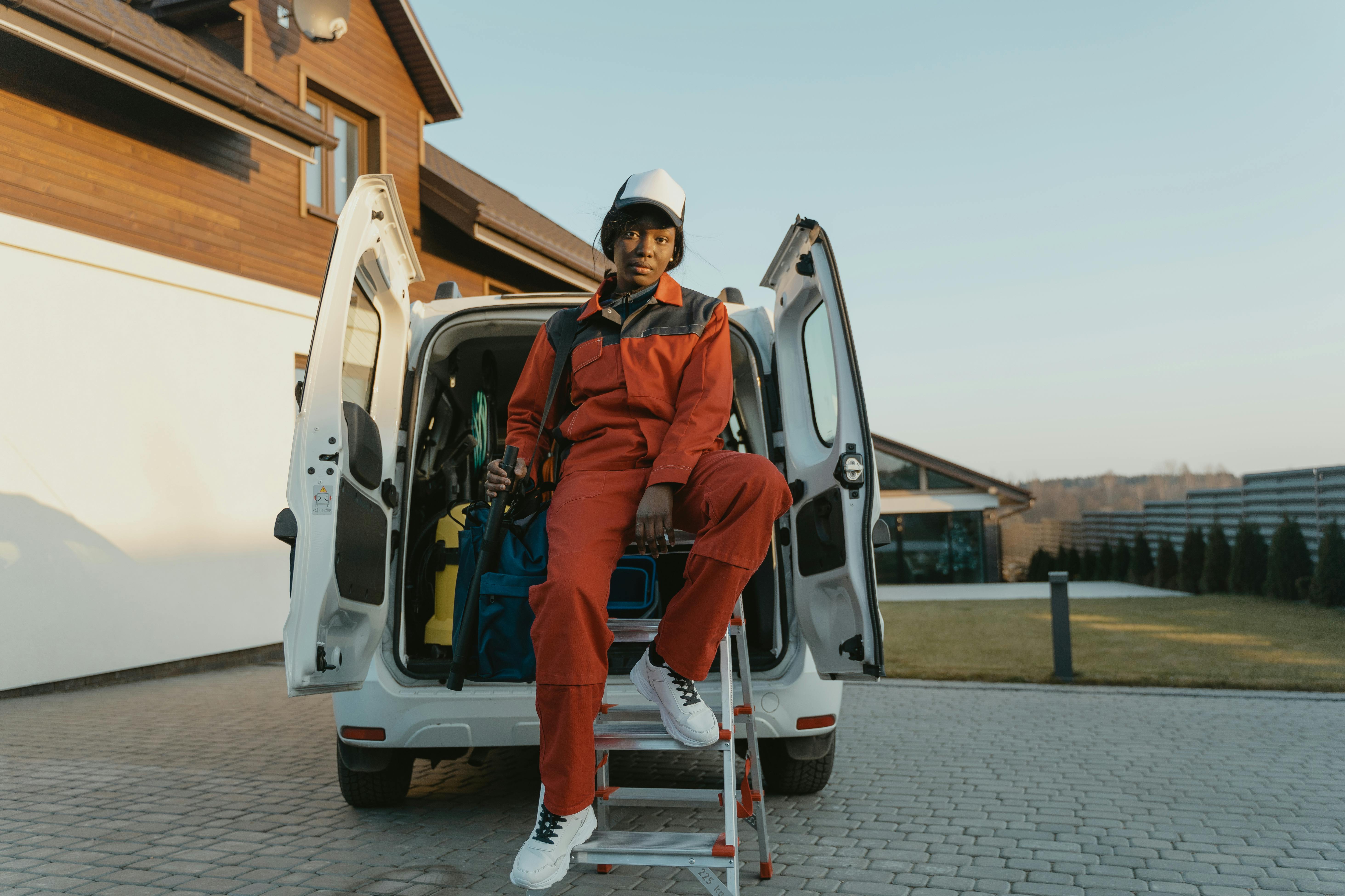 man in orange jacket and white pants wearing white helmet standing beside white van