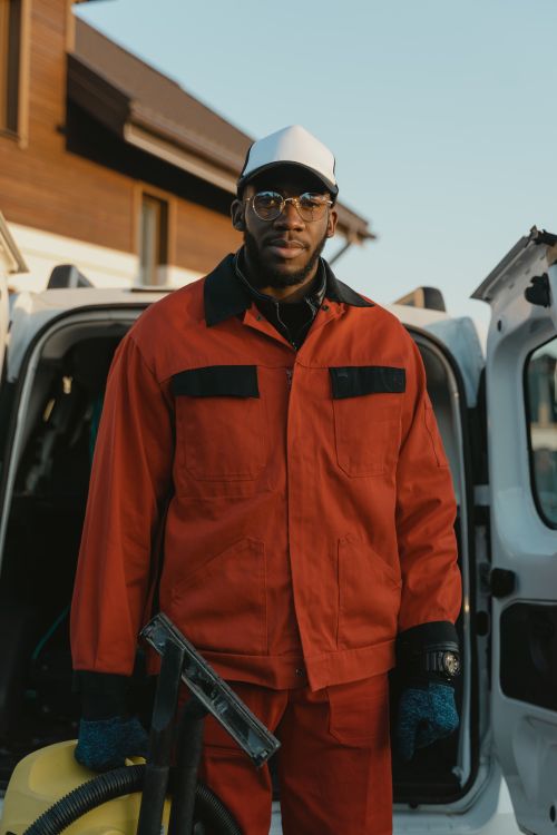 Free Man in red uniform standing by a vehicle, representing professional cleaning services. Stock Photo
