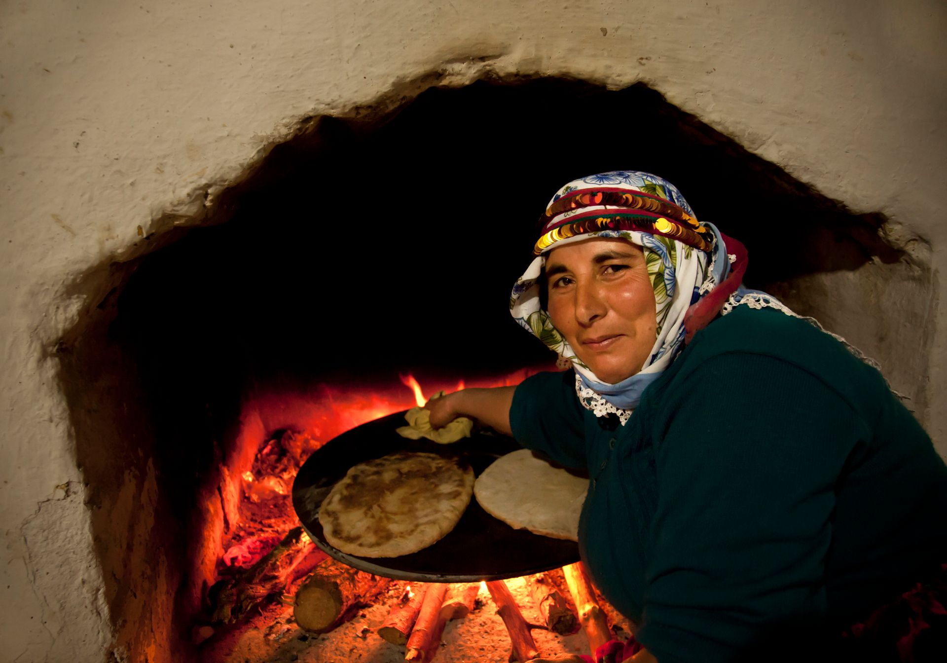 A woman in traditional attire baking flatbread in a Turkish stone oven, showcasing cultural cooking methods.