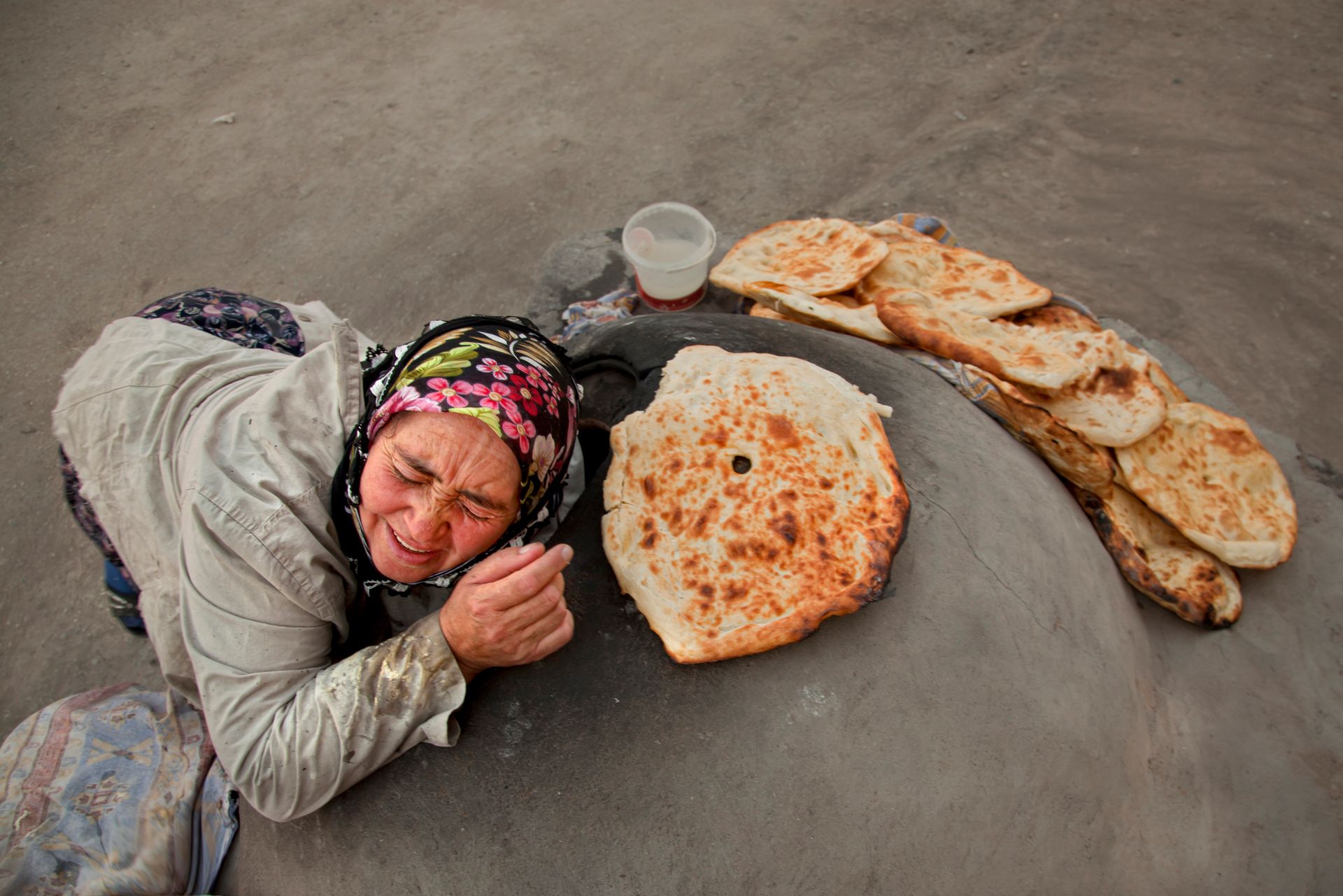 An elderly woman baking traditional bread in a stone oven in Türkiye.