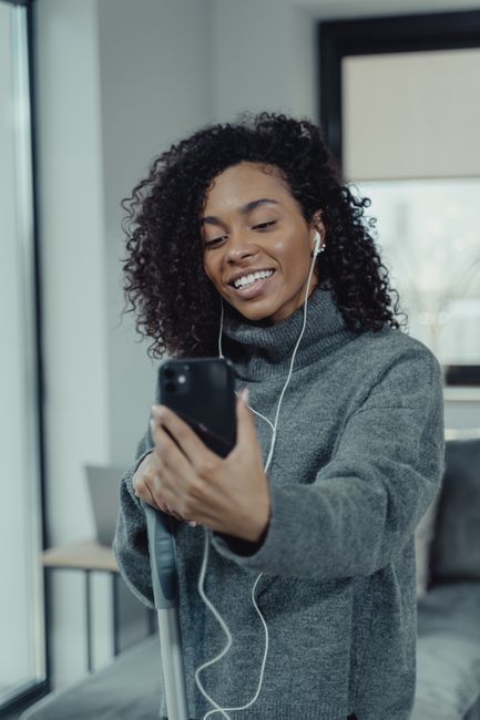 A joyful woman in a turtleneck sweater smiling during a video call on her smartphone at home