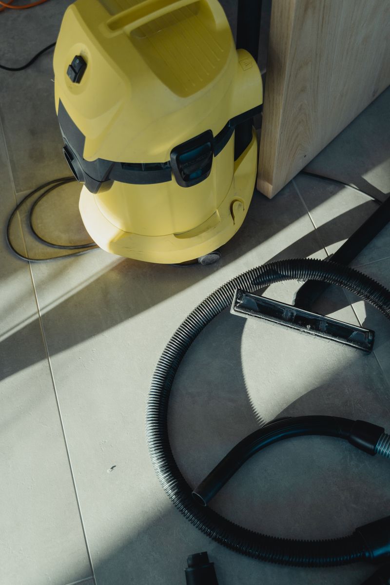 A yellow industrial vacuum cleaner with hose in bright sunlight on tiled flooring