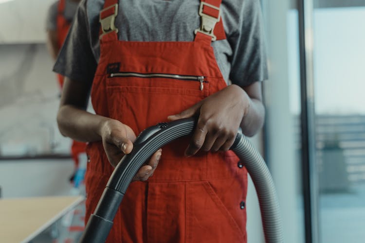 A Person In Orange Jumper Holding A Vacuum Hose