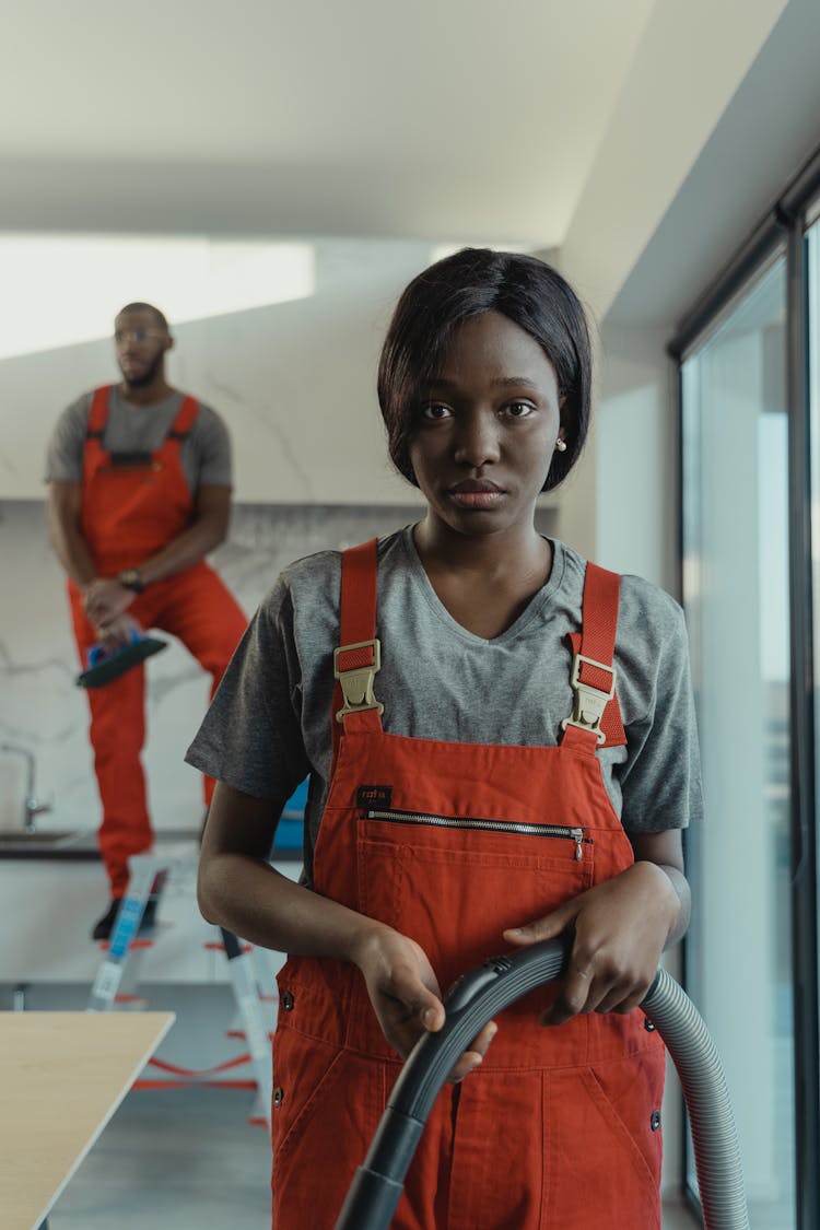 A Woman In Orange Jumper Holding A Vacuum Hose