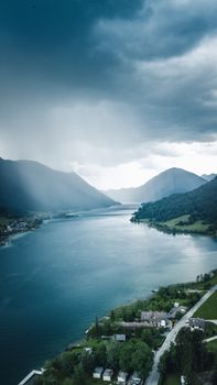 Capture of Weißensee, Austria showcasing dramatic clouds over serene lake surrounded by mountains and vivid landscape.