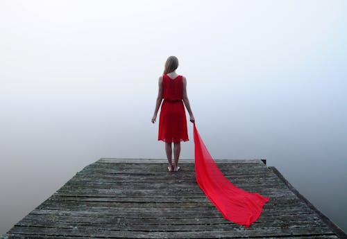 Back View of a Woman in Red Dress Standing on a Wooden Dock