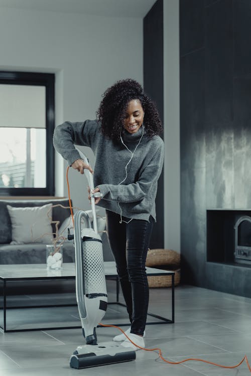 Woman in Gray Sweater and Blue Denim Jeans Standing Beside Black and White Luggage Bag