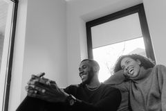 Black and white image of a smiling couple enjoying a moment indoors on a cozy sofa.