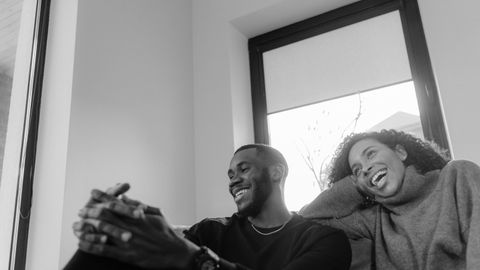 Black and white image of a smiling couple enjoying a moment indoors on a cozy sofa.