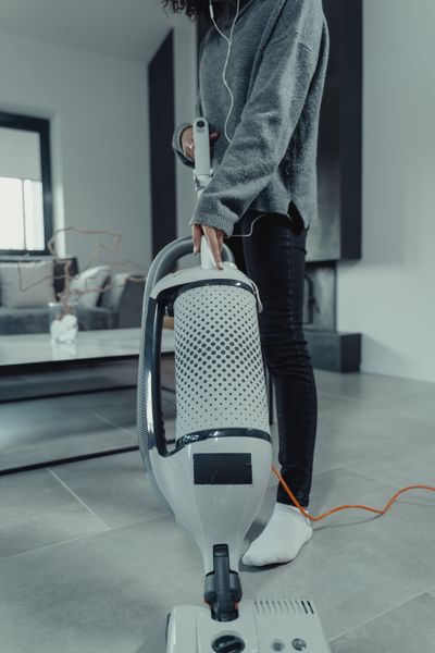 Cropped view of a person vacuuming a tiled floor beside living-room furniture