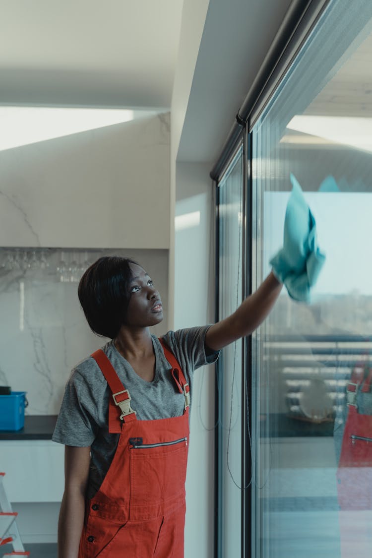 A Woman In Gray Shirt Wiping The Window