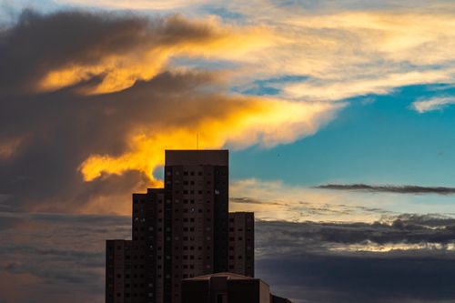 Free High dwelling concrete building under clouds lightened by sunlight floating on sunset sky in evening Stock Photo